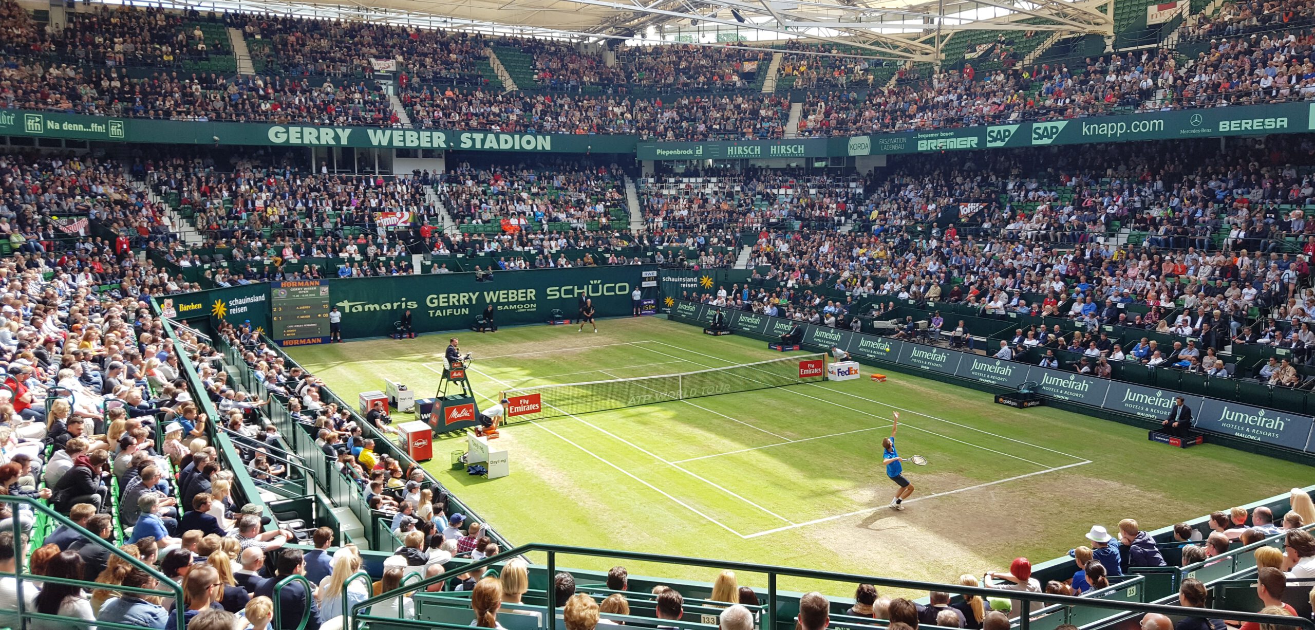 Vollbesetzte Zuschauertribünen von TS_Tribünen in einem Tennis-Stadion.